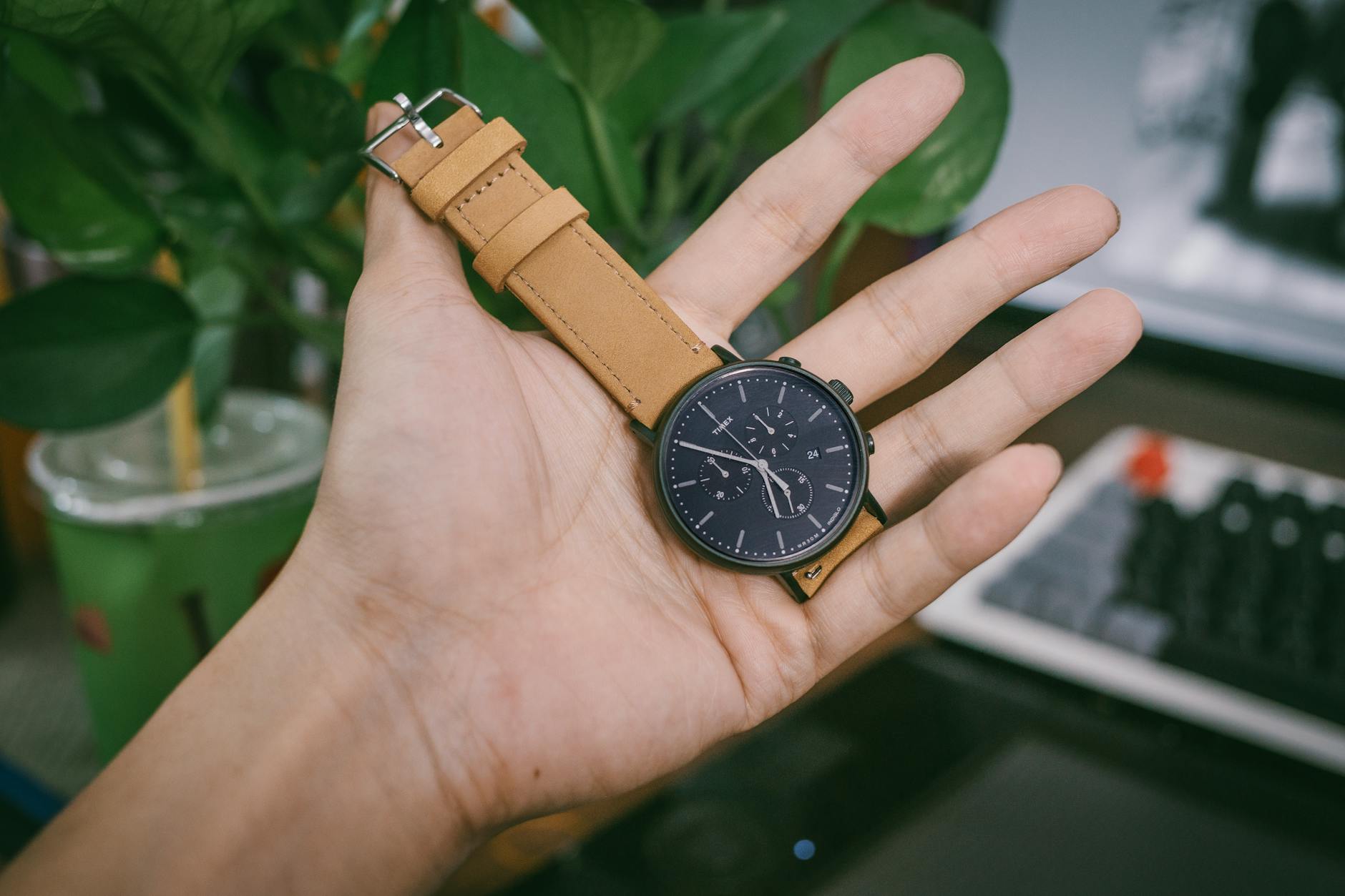 person holding black chronograph watch with brown leather strap